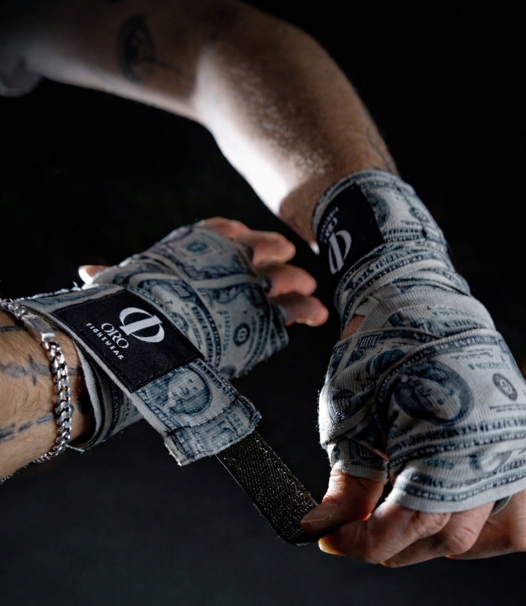 Manos con vendas Dollar y parches ORO Fightwear sobre fondo negro, ajustando el velcro