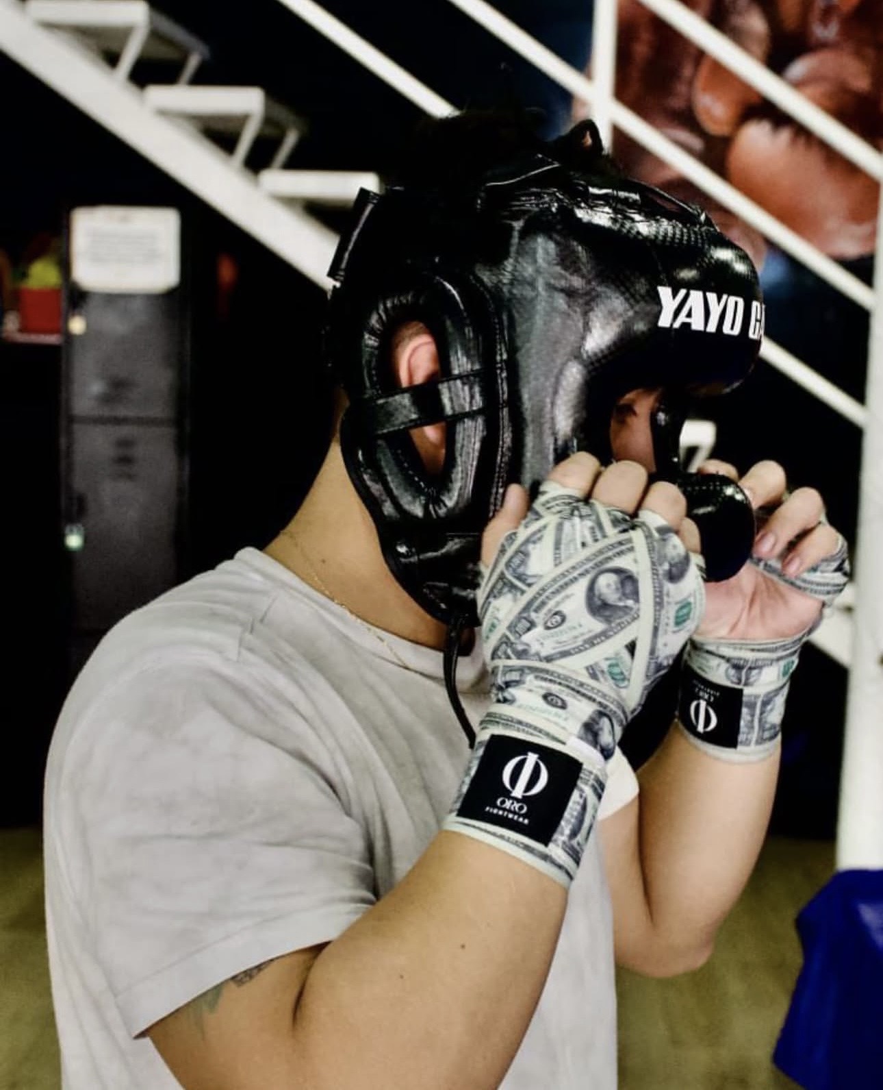 Boxeador con casco protector ajustando sus vendas Dollar en el gimnasio